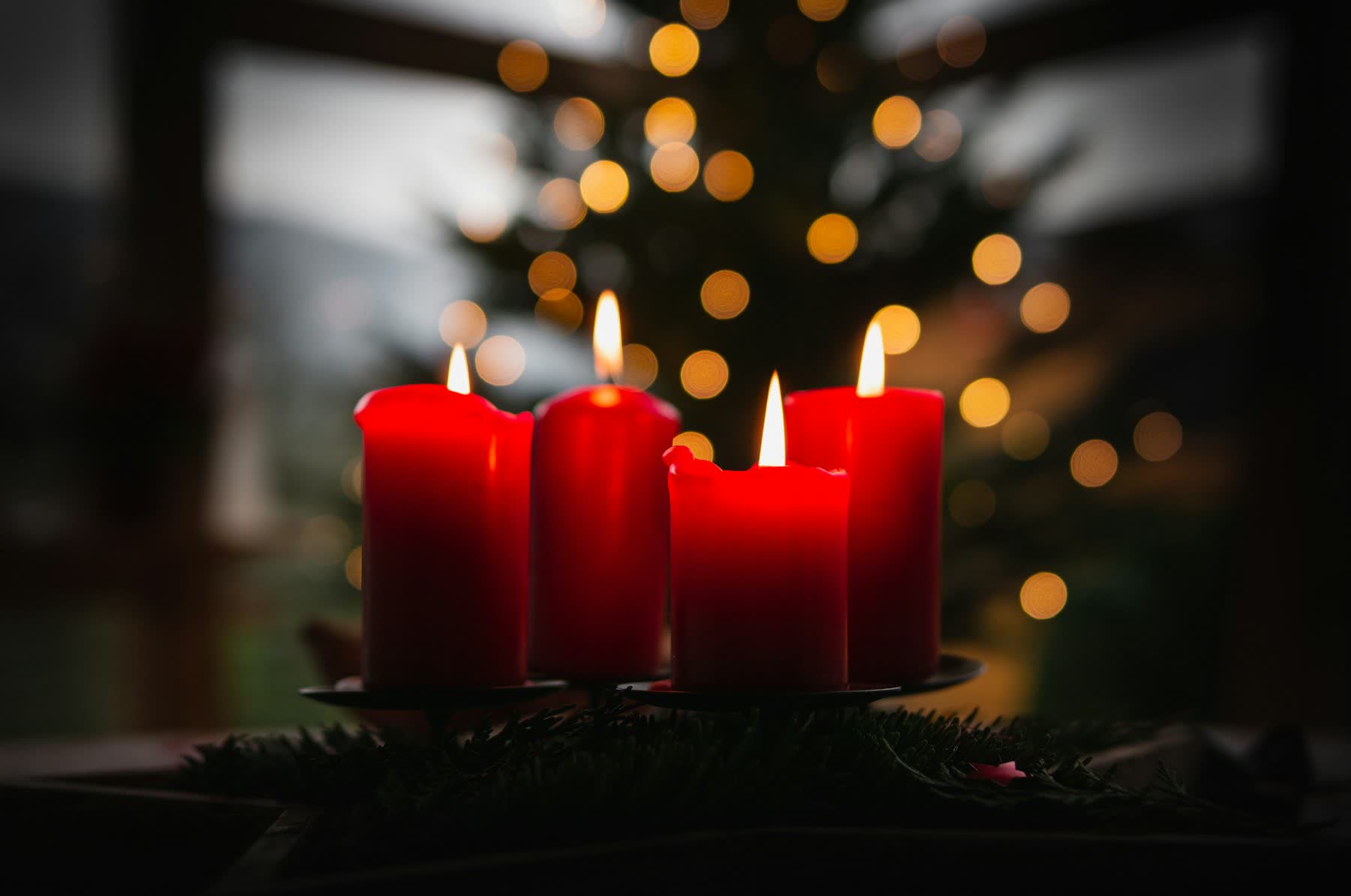 Crvene svijeće adventskog vijenca uz svjetla božićnog drvca